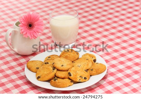 Plate of cookies with glass of milk and flower on checked tablecloth.