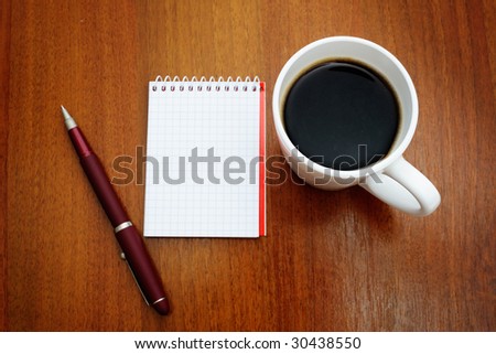 Pen on a white spiral squared notebook with cup of coffee viewed from above