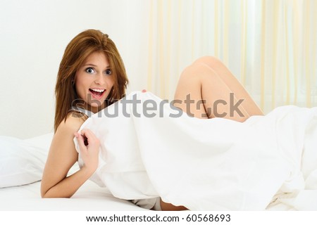 Young woman laughing and covering her body with a bed sheet