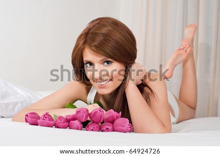 Happy girl laying on the bed with bouquet of tulip