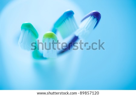 Close-up of four multicolored toothbrushes in white holder against blue background, Blue gel filter was used.