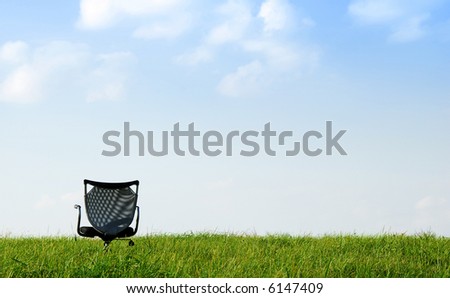 A office chair on a green meadow with blue sky and clouds