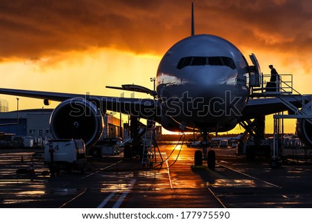 Airplane silhouette, storm cloud low ceiling during sunset on background, look like fire