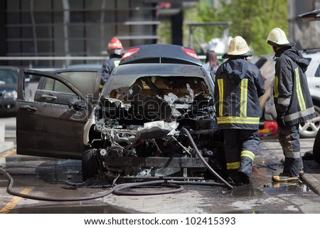 A burnt car and fire fighters around it