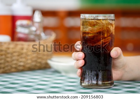 Hand holding glass of cola drink on table with restaurant background