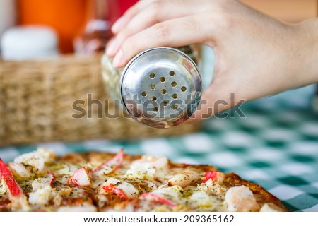 Shaking oregano spices on pan of pizza with restaurant background