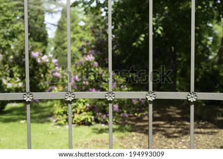 An image of a flower garden protected by an iron fence with crafted handiwork