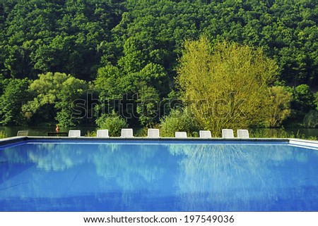 Image of an outdoor swimming pool against a backdrop of river and forest