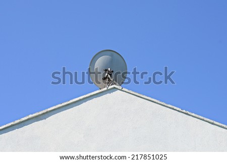 Image of a satellite dish sitting high at the apex of a white roof against a deep blue sky with room for copy space