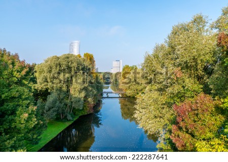 Image of a river lined by trees and tall buildings in the distance