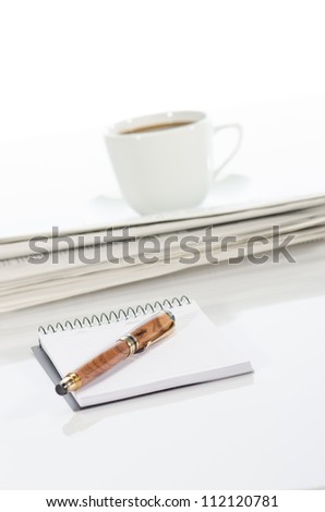 Cup of coffee, pen, notebook and newspaper against a  white background