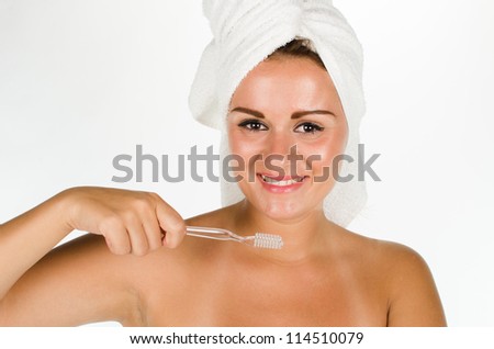 Portrait of young woman after bath brushing her teeth against white background