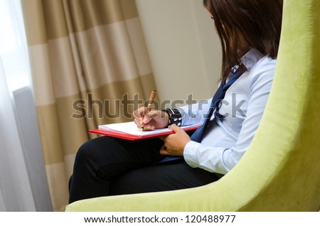 Young businesswoman sitting in a armchair and writing on clipboard