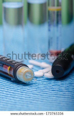 Insulin pen, vials and pills on blue surface