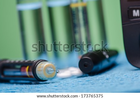 Insulin pen, vials and pills on blue surface