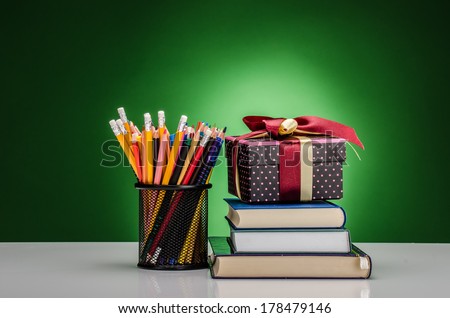 Crayons, markers, books and a present against green background