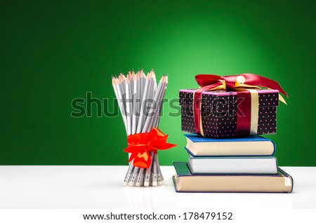 Pencils, books and a present against green background