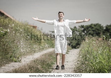 Happy young man with open arms in a field  under  the summer  sun