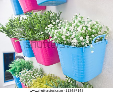 Plastic flowers with colorful plastic vases hang in row on the wall.