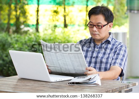 Asian man reading the financial newspaper with white laptop.