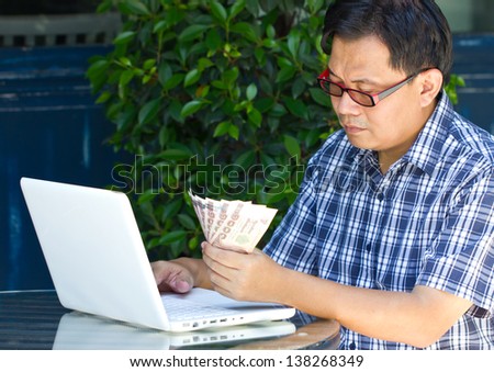 Asian man with laptop and his thai bank note.