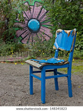 Old blue chair in the open air surrounded by green and graffiti