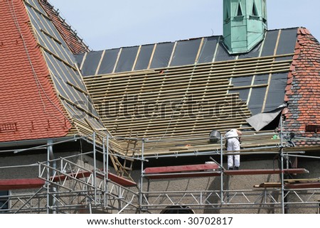 Roof construction works. Worker and scaffolding. Building renovation.
