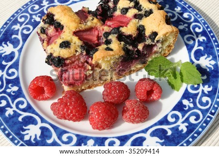 Slice of berry cake and raspberries on a decorative blue porcelain plate