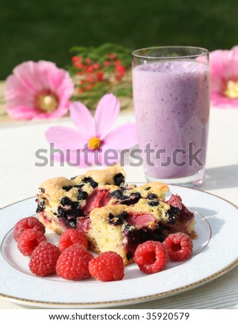 Slice of berry cake and raspberries on a decorative porcelain plate. Fruit milk shake in background.