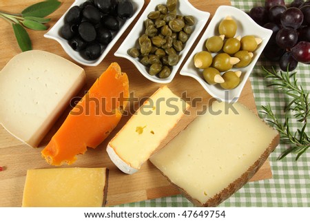 Varieties of hard cheese on a wooden board. Grapes, olives and other pickled ingredients.