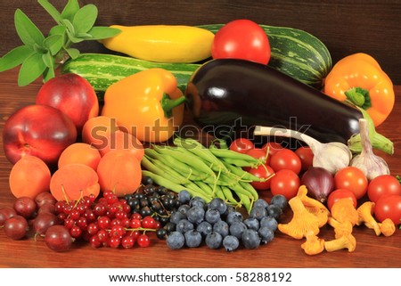 Various fresh fruits and vegetables on a wooden table: tomatoes, beans, courgettes, aubergine, garlic, onion, chanterelles, apricots, nectarines, red and black currants, blueberries and gooseberries.