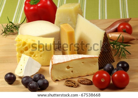Varieties of hard cheese on a wooden board. Grapes, tomatoes, rosemary and nuts.