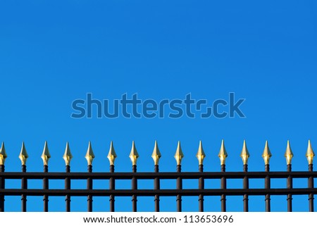 Top part of old beautiful metallic fence with gold tips on sky-blue background