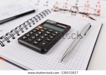Calculator, datebook, metallic pen, glasses and calendar on white