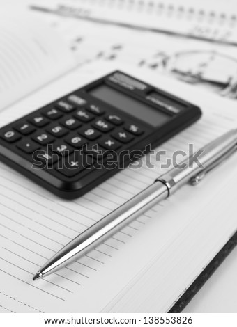 Datebook, metallic pen, calculator, glasses and calendar. Black and white picture.