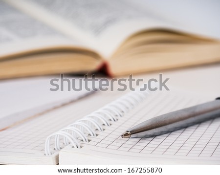 Metallic pen, spiral squared paper notebook and opened book