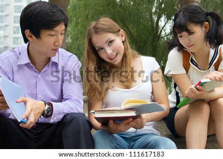 Group of college students holding books. American and Asian teenagers studying outside of university campus
