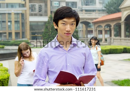 Portrait of young Asian man student carrying book outdoors and smiling. Teenagers lifestyle outside of university campus