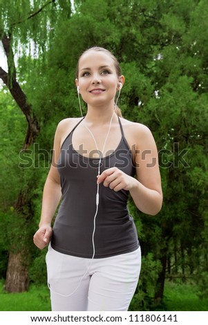 Beautiful young woman run and listen music in green park with music. Woman fitness jog workout wellness concept