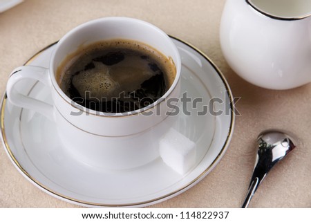 Strong black freshly brewed coffee in a cup and saucer with spoon and a small milk jug to the side