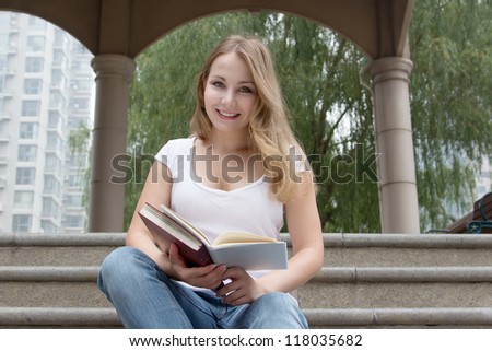 Student girl outside in summer green park smiling happy. Caucasian female college or university student sitting on stairs and study