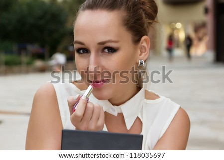 Young woman applying cosmetics make-up, putting on lipstick