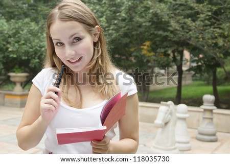 Portrait of happy smiling woman with book on green background with chessmen playground of city park