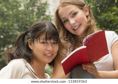Young beautiful happy women reading book at city park. Girls smiling and have fun outdoor