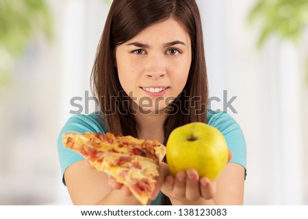 Young woman holding different food and selecting fat pizza or low calorie apple, healthy lifestyle and diet concept