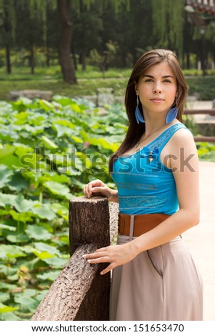 Cute girl on the bridge near pond with pink lotus, young woman walking in the lotus park