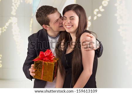 Young man hugging his girlfriend and offering a gift, young couple laughing together