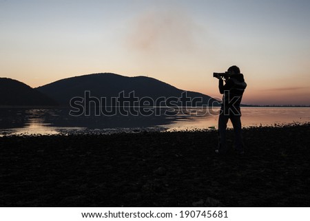 Photographer silhouette/A back lit figure of a photographer with his lens pointed towards a sunset landscape near a lake. Romania, Negresti Oas, November 11, 2011