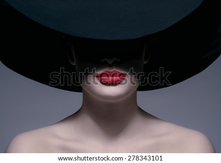 young woman in a black hat without a face with red lips smiling shoots in studio
