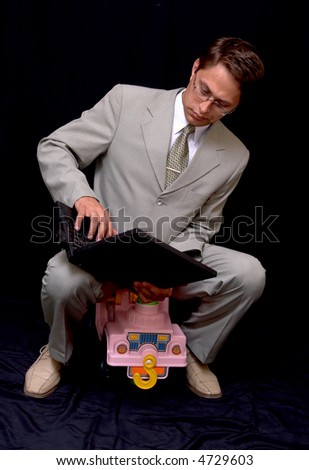 The businessman works on the computer sitting on the children's automobile